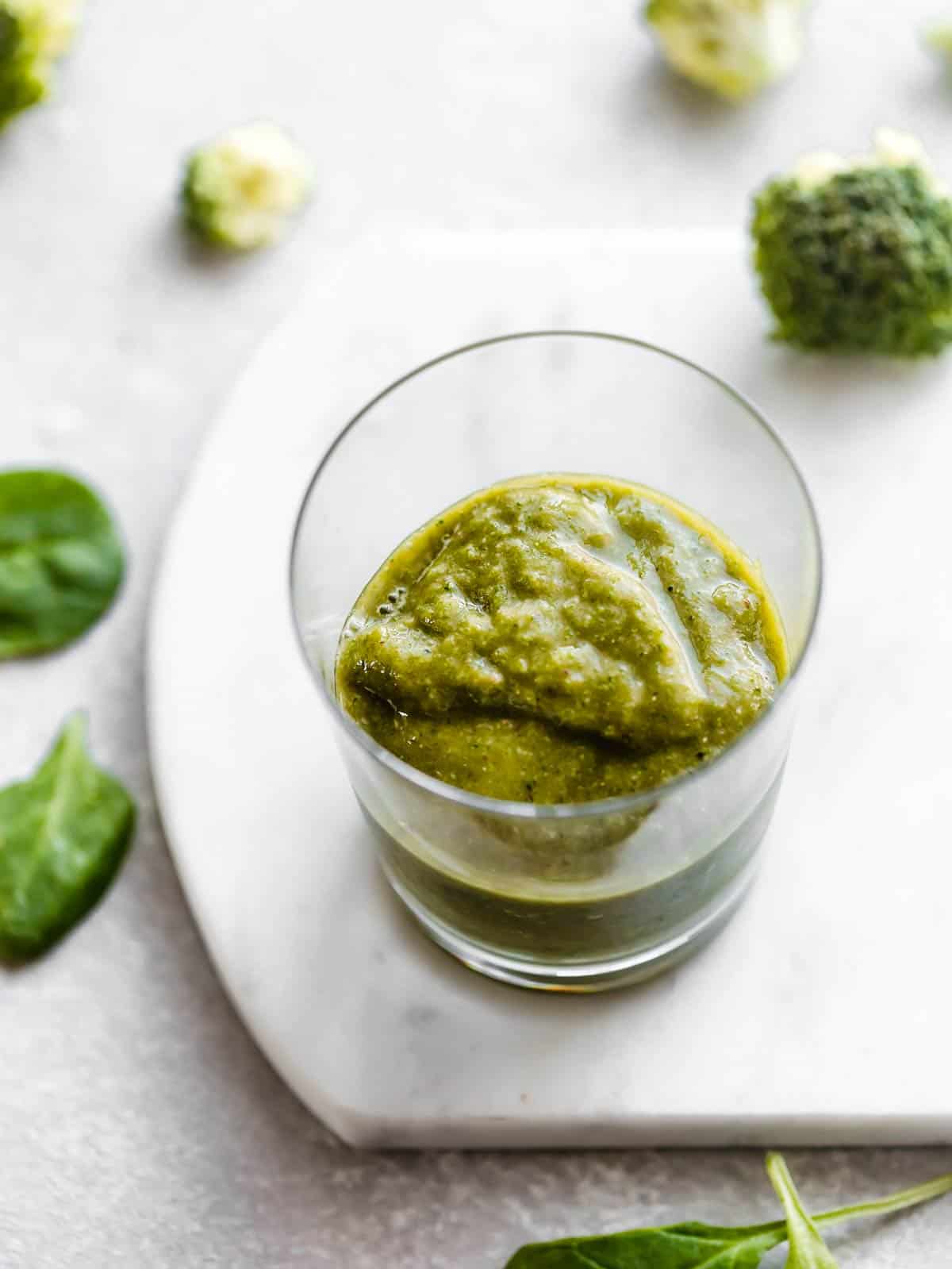 A clear cup half full of Broccoli Smoothie on a white background.