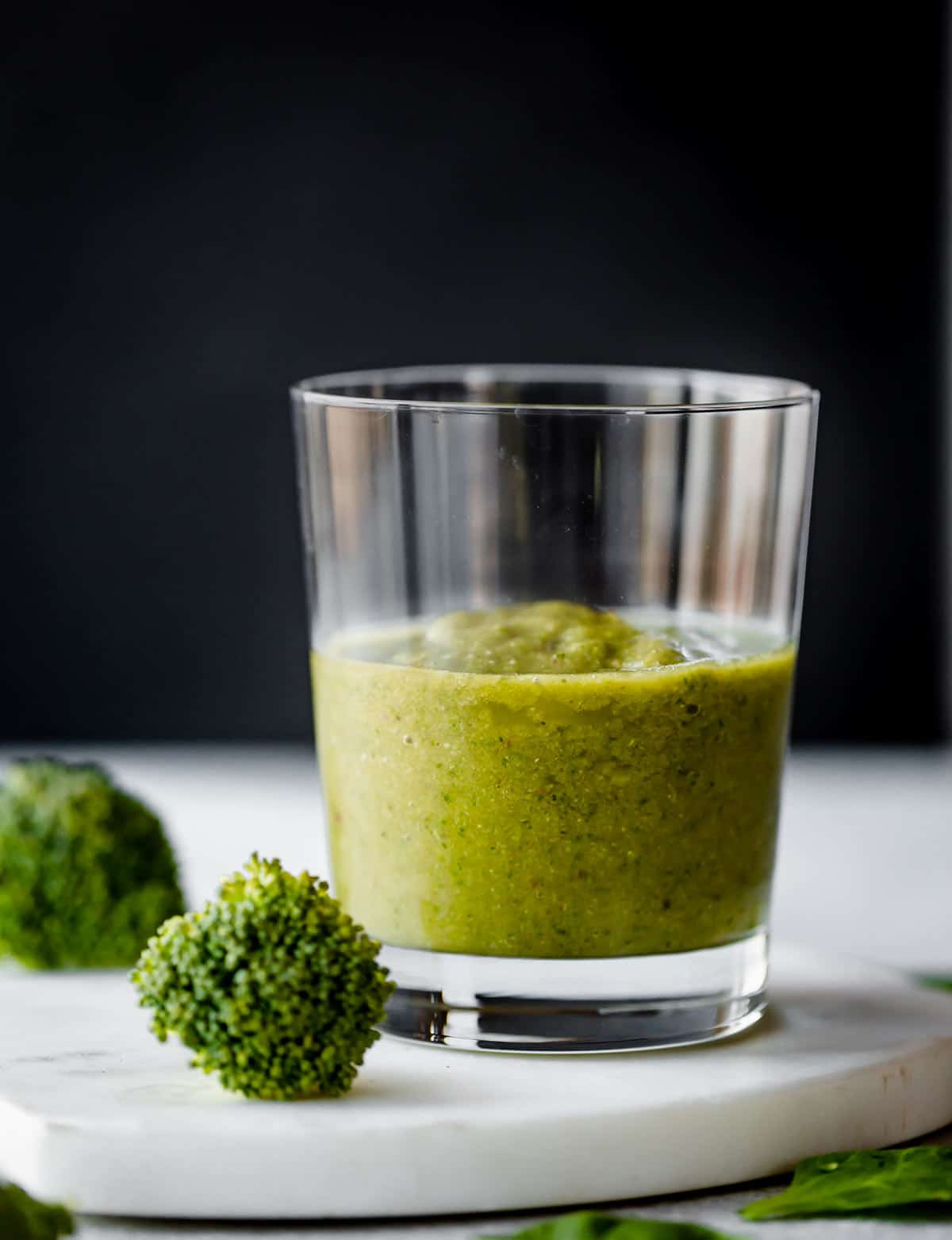 Broccoli Smoothie in a clear cup against a black background.