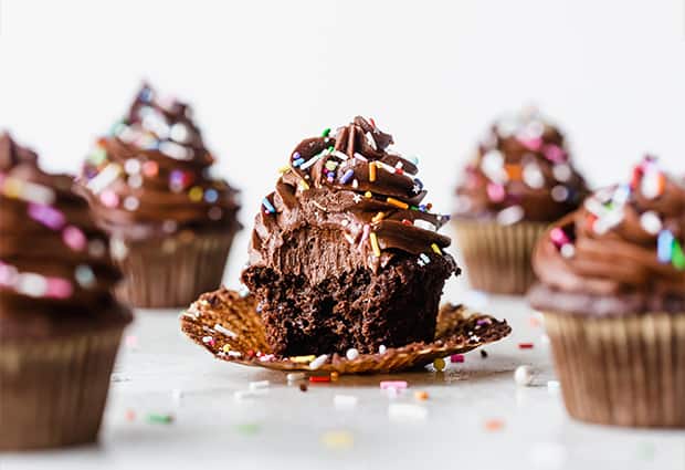 The best chocolate cupcake topped with chocolate buttercream frosting and colorful sprinkles, with a large bite taken out of the cupcake.