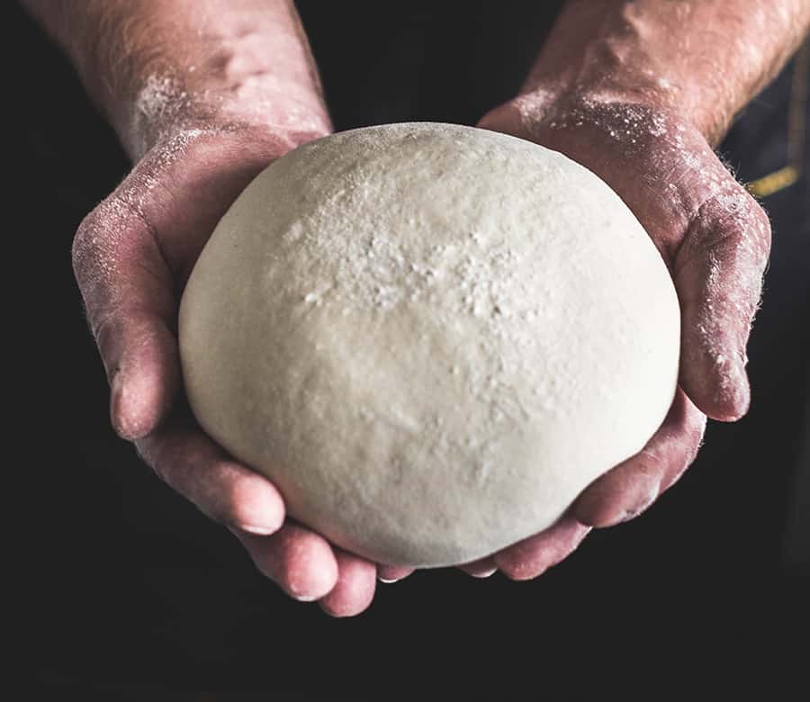 A mans hands holding a ball of dough.