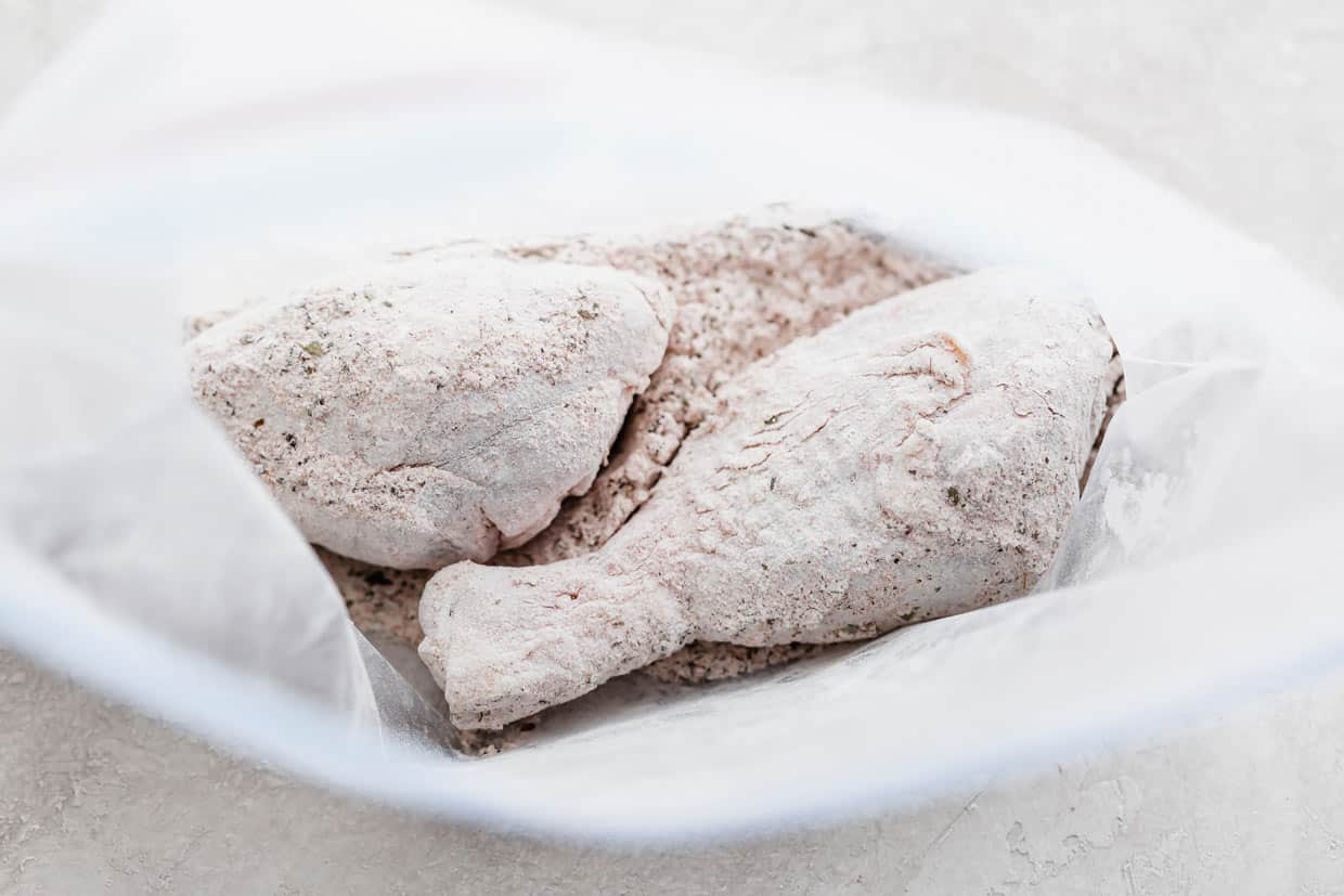 Two flour and cornstarch coated chicken legs in a ziplock bag.