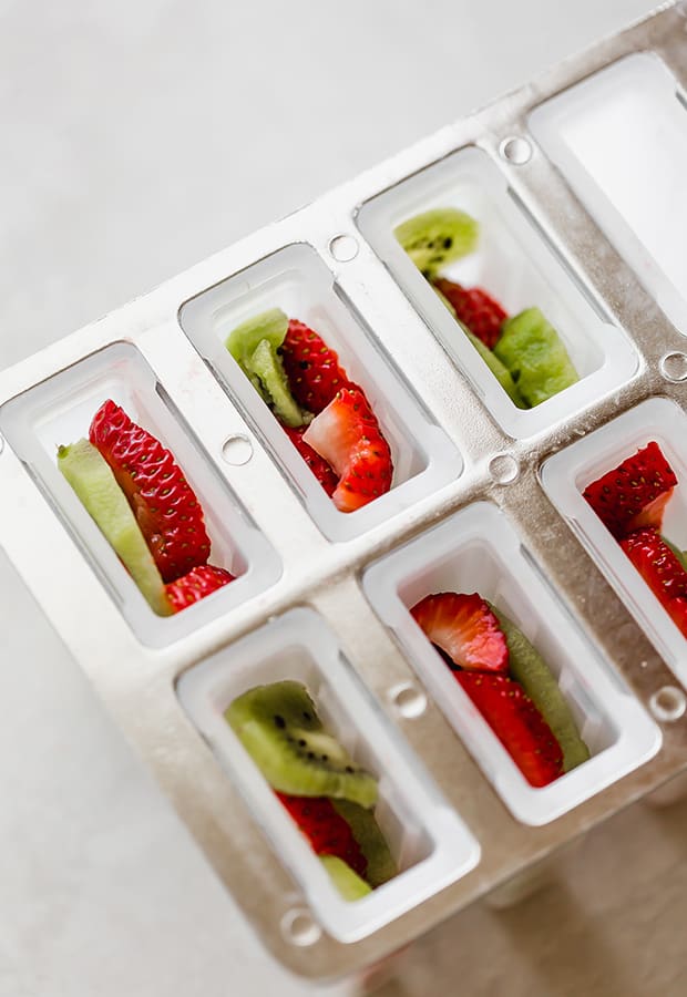 Popsicle molds filled with sliced kiwis and sliced strawberries.