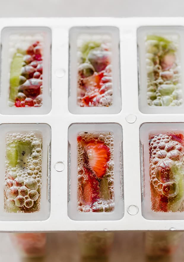 Popsicle mold full of sliced kiwis and strawberries and fizzy 7-Up.