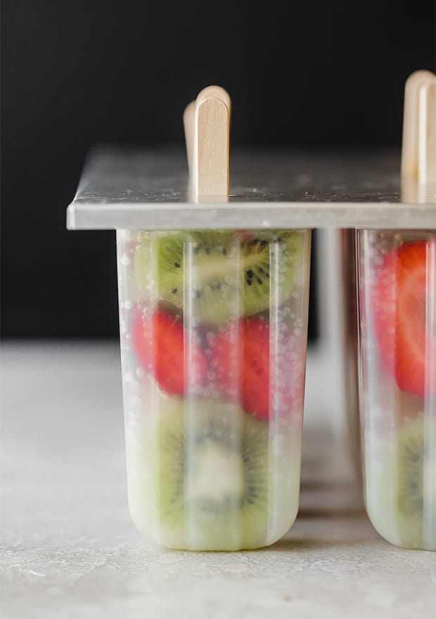 A popsicle mold full of sliced kiwis, strawberries, and 7-up.