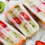 Kiwi strawberry popsicles sitting on a pile of frozen ice cubes.