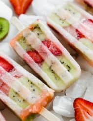 Kiwi strawberry popsicles sitting on a pile of frozen ice cubes.