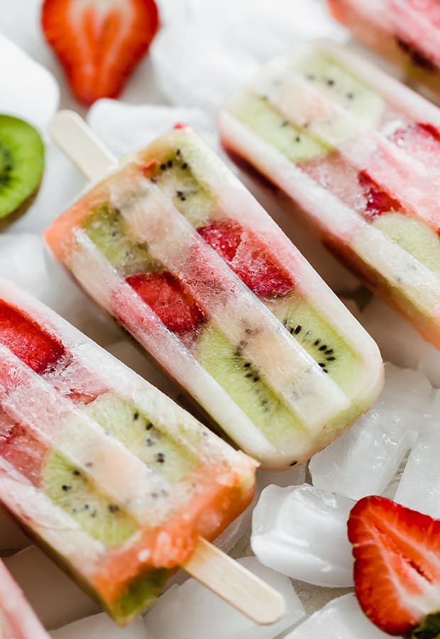 Kiwi strawberry popsicles sitting on a pile of frozen ice cubes.