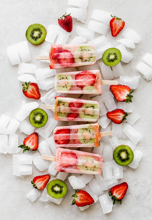 Five kiwi strawberry popsicles on top of a pile of ice cubes.
