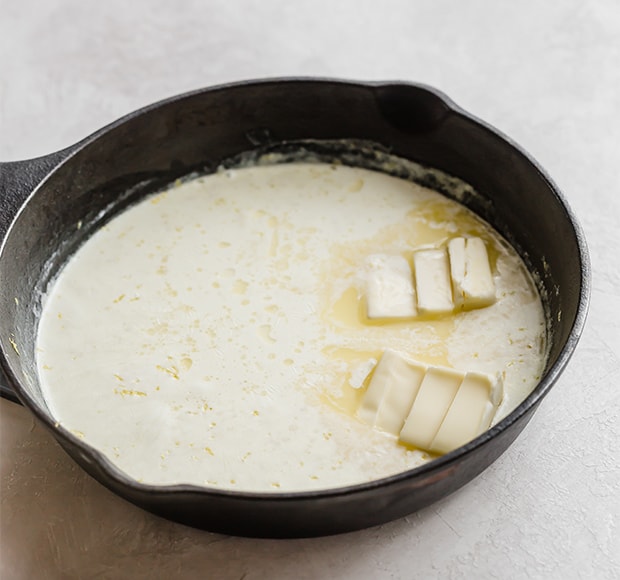 A skillet with heavy cream and butter slices in it.