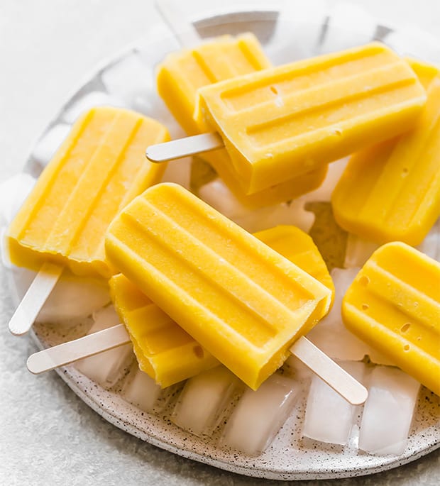 A plate covered in ice, and pineapple mango popsicles laying on top of the ice.