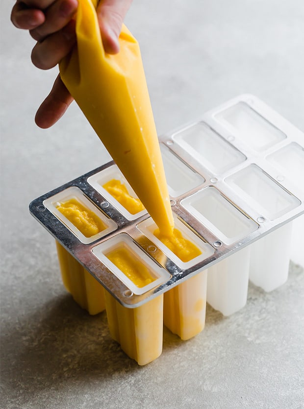 A pastry bag filling the popsicles molds with the pineapple mango puree.