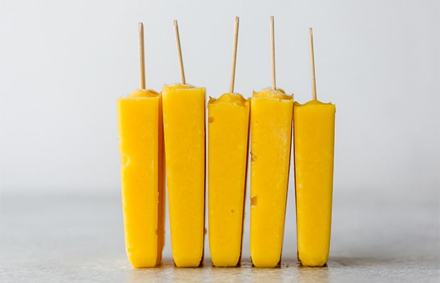 Five pineapple mango popsicles standing on its ends lined up by each other.