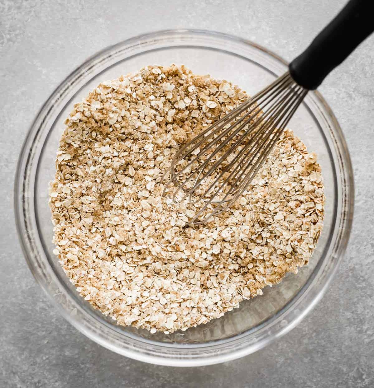 A whisk stirring quick oats in a glass bowl.