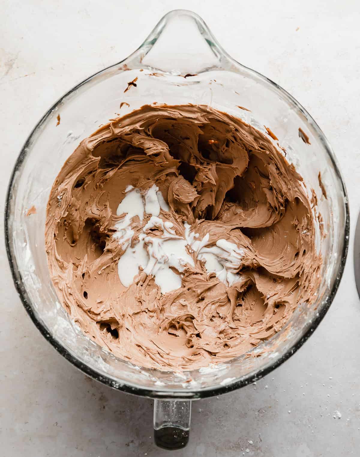 Heavy cream poured over top a light brown Chocolate Buttercream Frosting in a glass bowl.