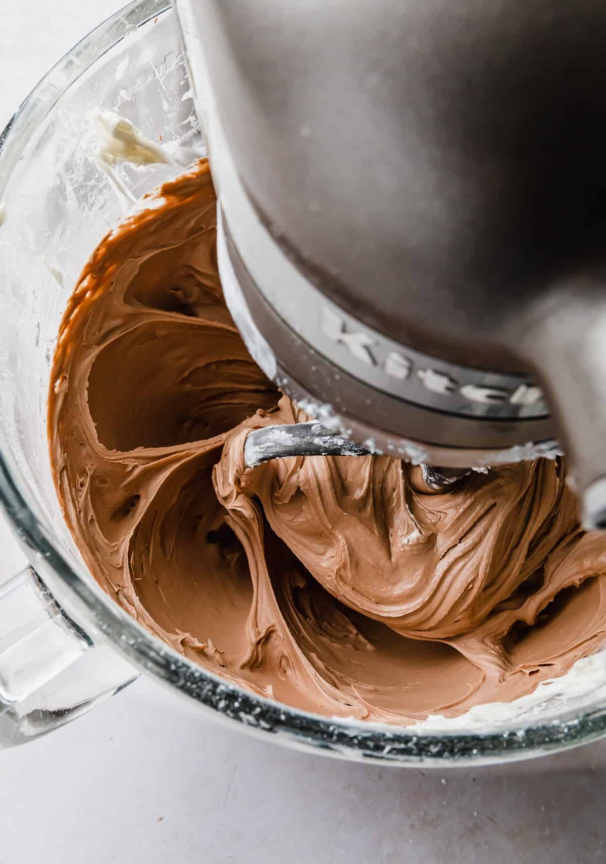 Chocolate Buttercream Frosting with Melted Chocolate being stirred in a glass kitchen aid bowl.