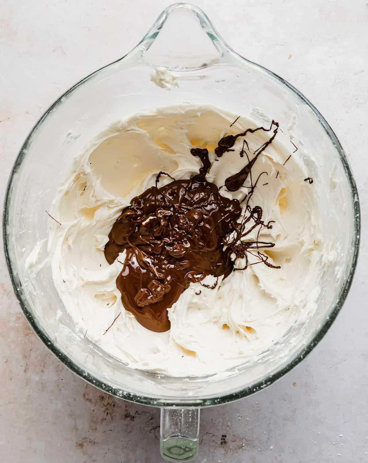 Creamed butter and powdered sugar in a stand mixer bowl with melted chocolate poured overtop.