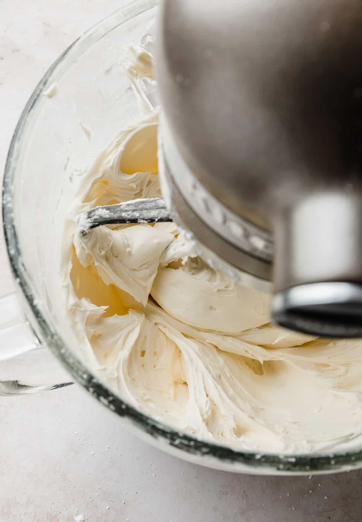 White frosting being mixed in a stand mixer bowl with a paddle attachment.