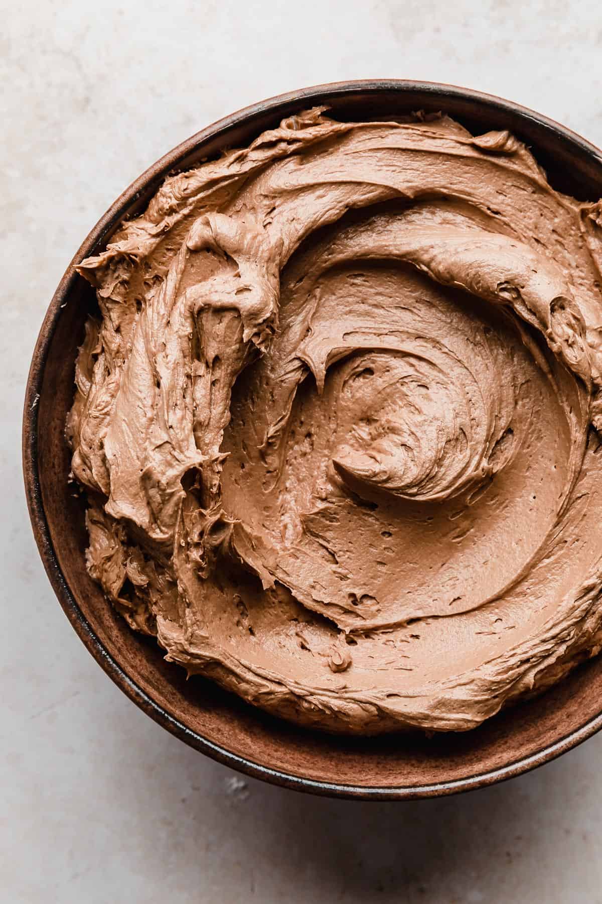 A brown bowl full of light brown colored Chocolate Buttercream with Melted Chocolate.
