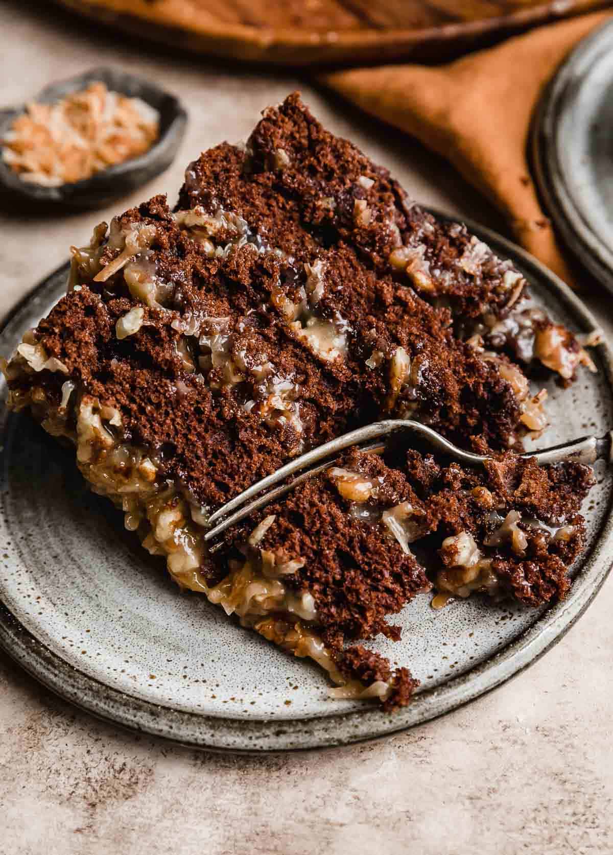 A slice of Traditional German Chocolate Cake made with sour cream, on a gray plate with a fork cutting into the cake.