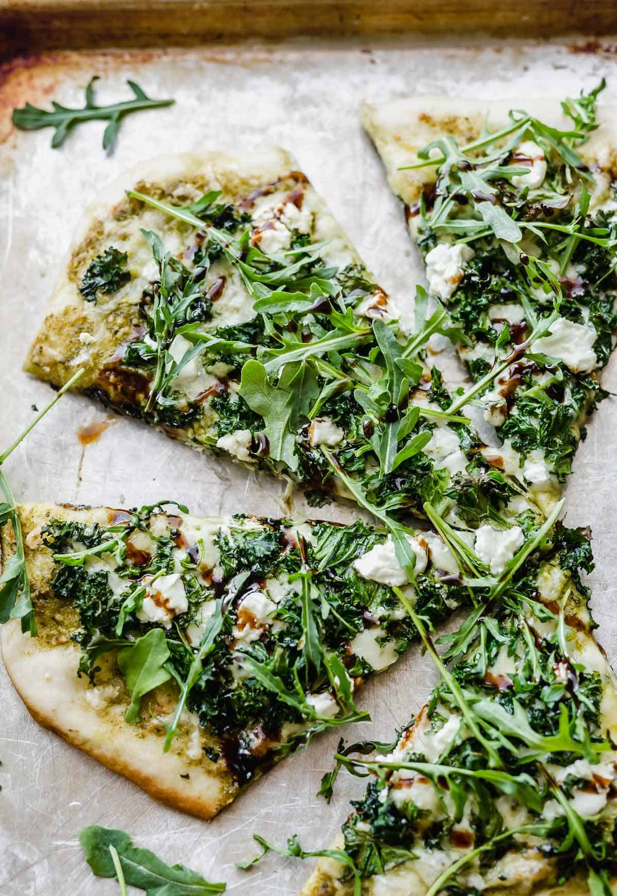 Kale pizza slices topped with arugula and goat cheese.
