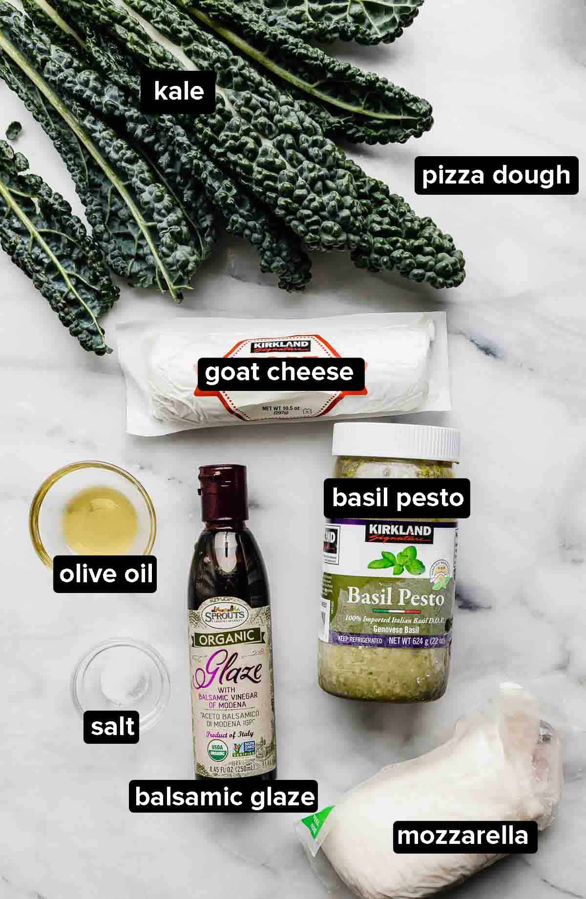 Kale Pizza ingredients (kale, olive oil, pesto, goat cheese, mozzarella) on a white marble background. 