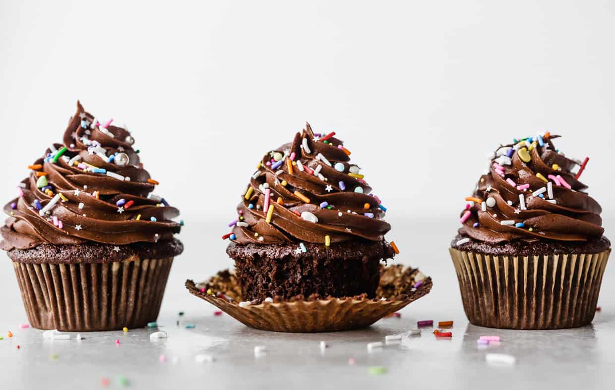 A row of three chocolate frosting topped chocolate cupcakes. 