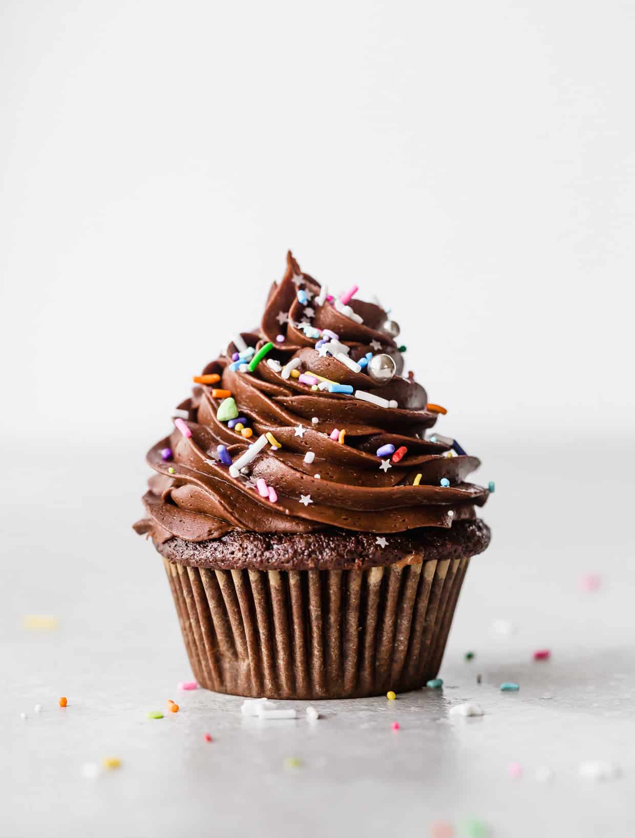 A single chocolate cupcake topped with a swirl of chocolate frosting and colorful sprinkles.