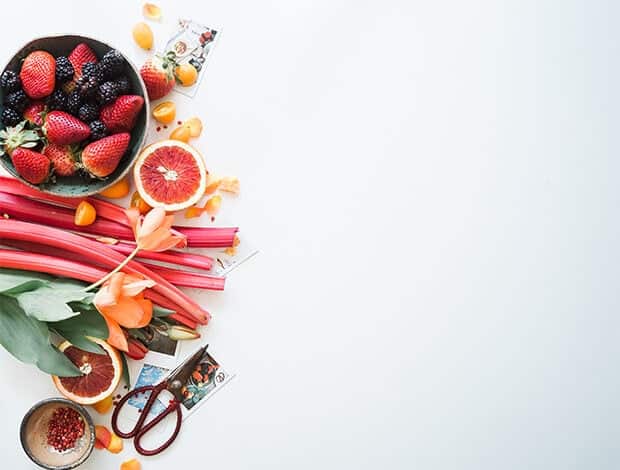 A spray of fruits light grapefruit, rhubarb, and berries hugging the left side of the photo.