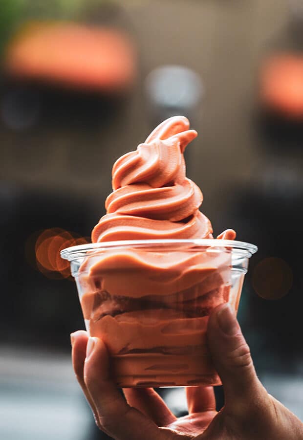 A hand holding a cup of pink/orange ice cream.