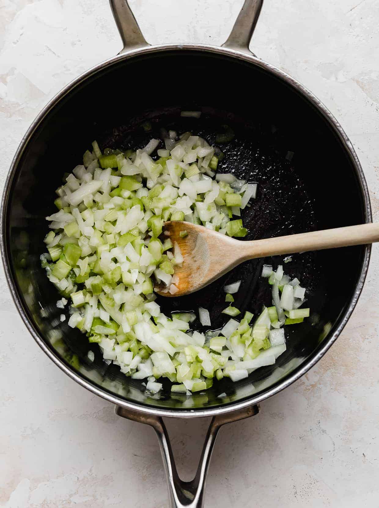 A saucepan with diced onion and celery in it.