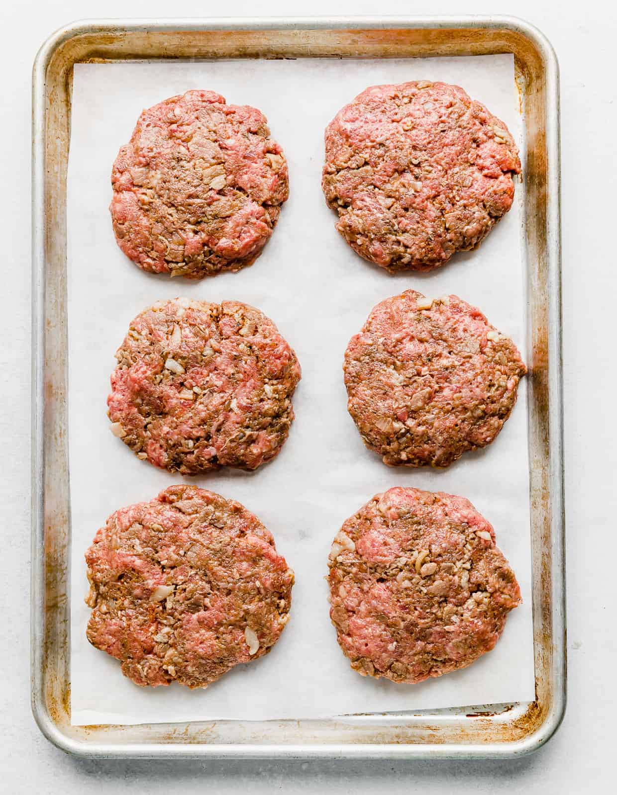 6 raw bacon burgers on a parchment lined baking sheet. 