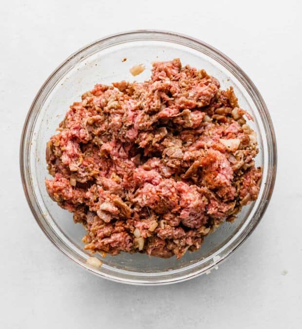 Mixed ground beef with seasoning in a glass bowl.