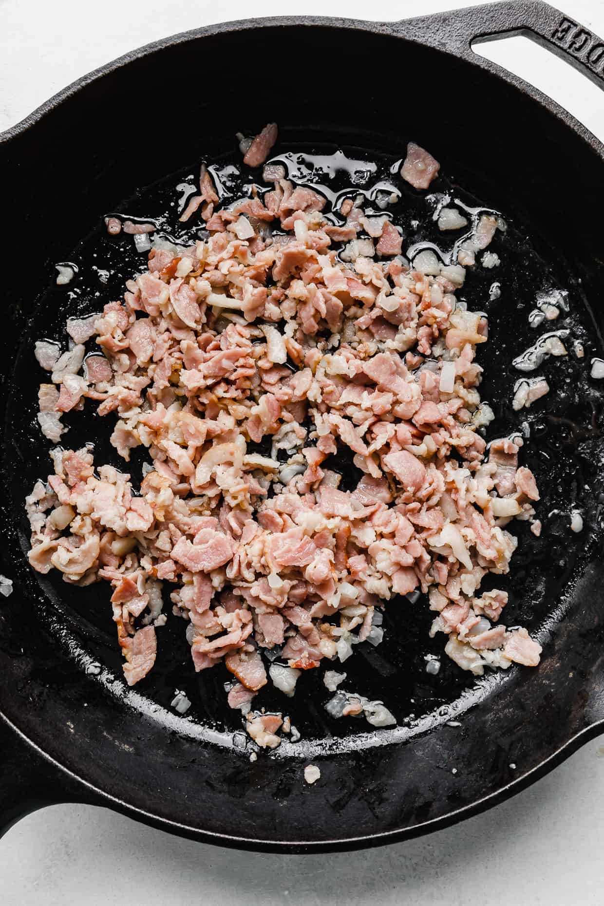 Slightly cooked bacon and diced onion in a cast iron skillet.