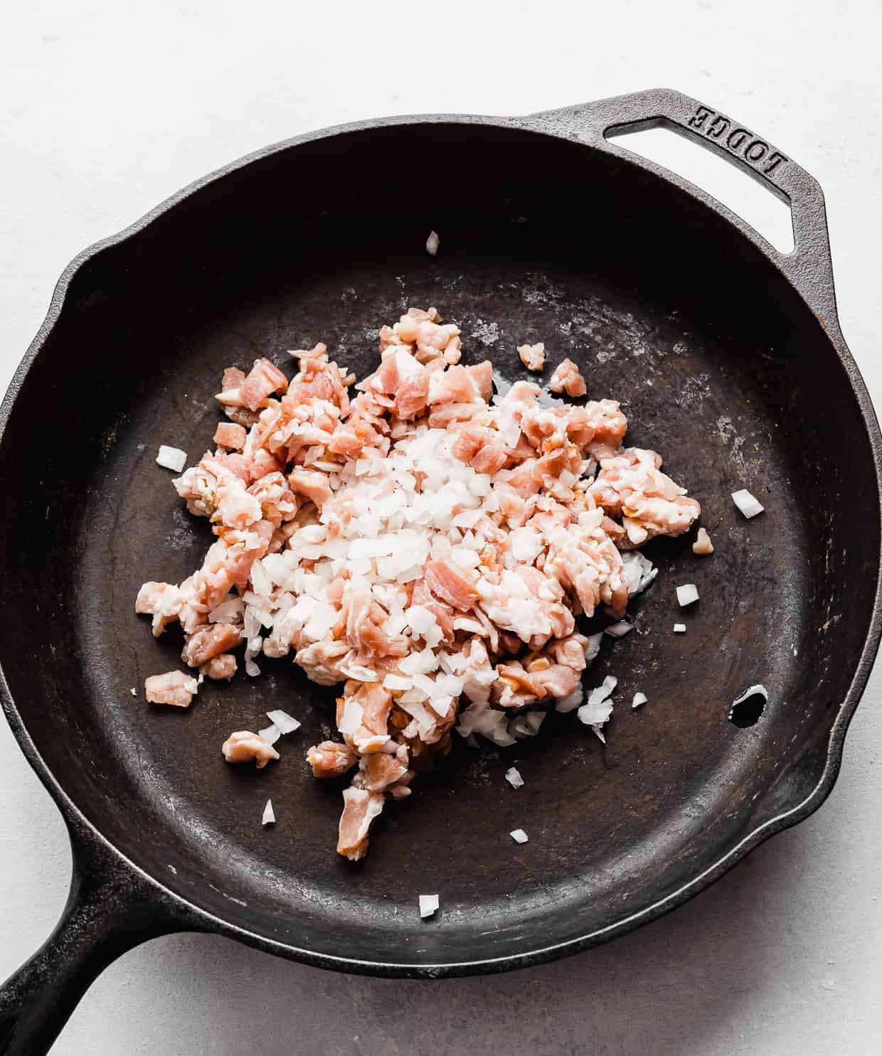 A black skillet with diced onion and diced bacon in it.