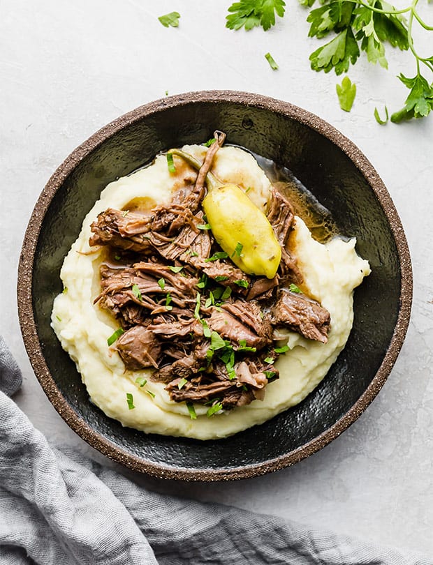 Overhead photo of Mississippi Pot Roast on a bed of mashed potatoes with a garnish of parsley.