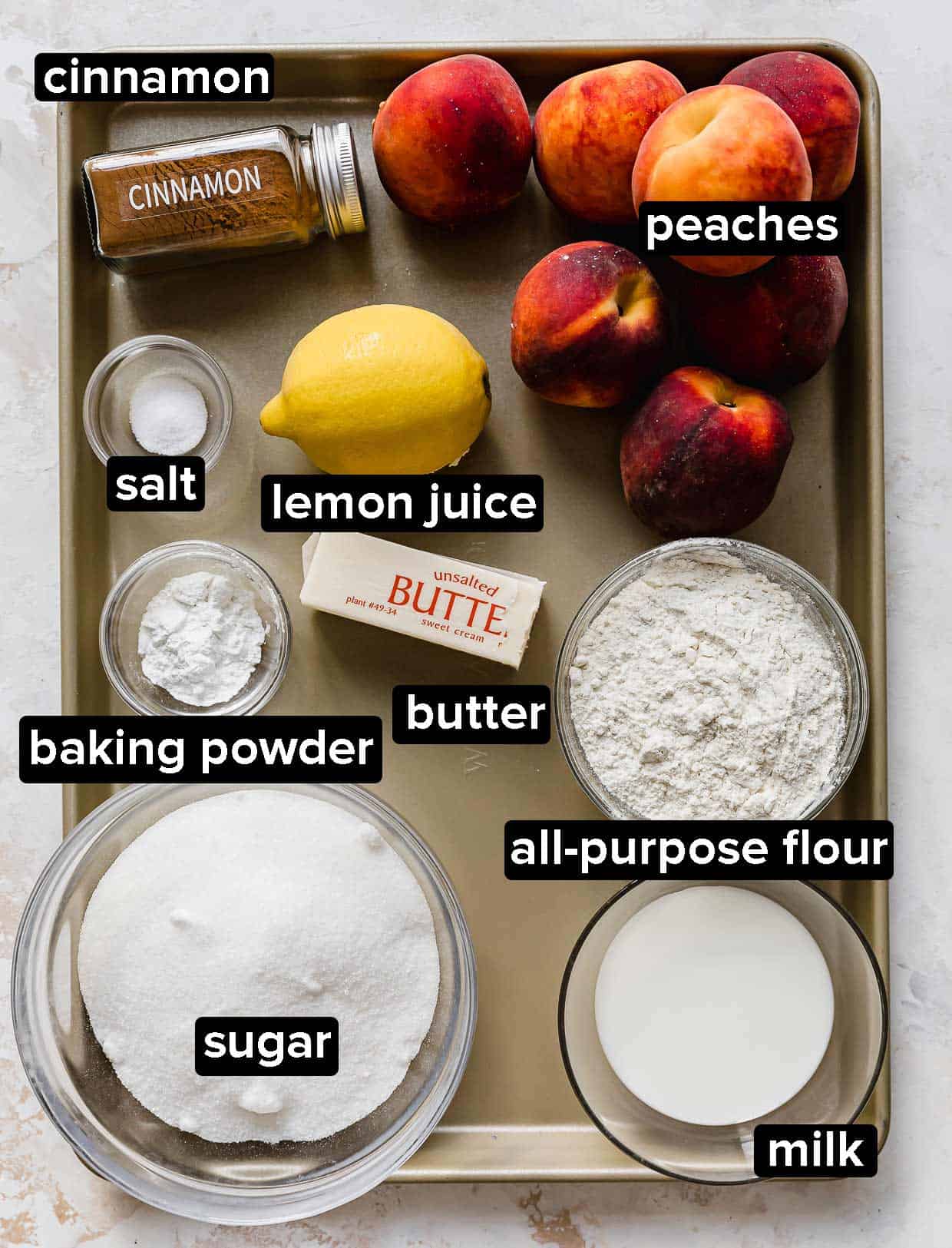 Peach Cobbler on a baking sheet: fresh peaches, butter, lemon, cinnamon, milk, sugar, flour, and baking powder.