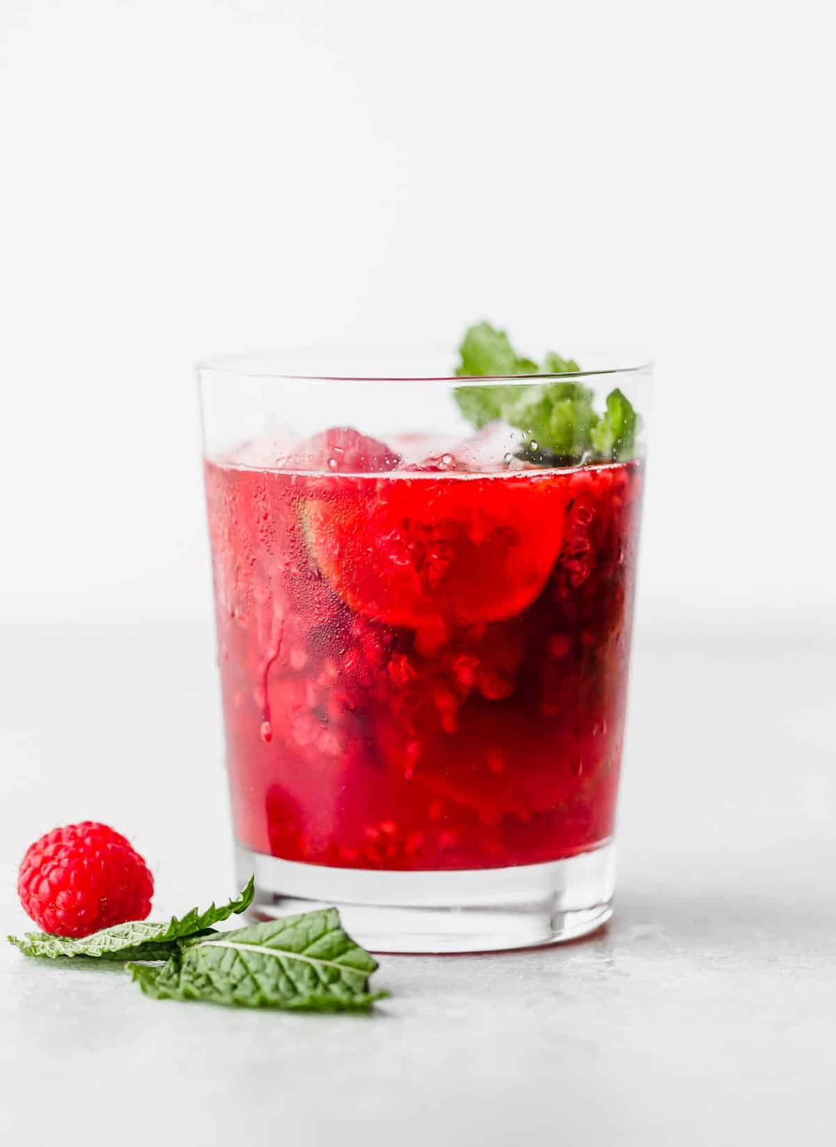 A glass of raspberry mocktail against a white background.