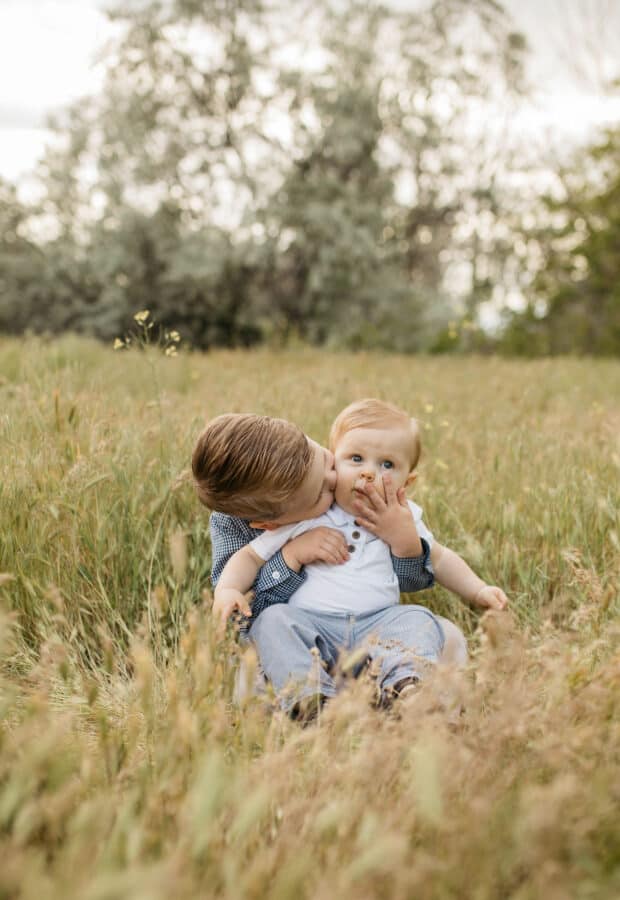 A boy kissing his baby brothers cheek.