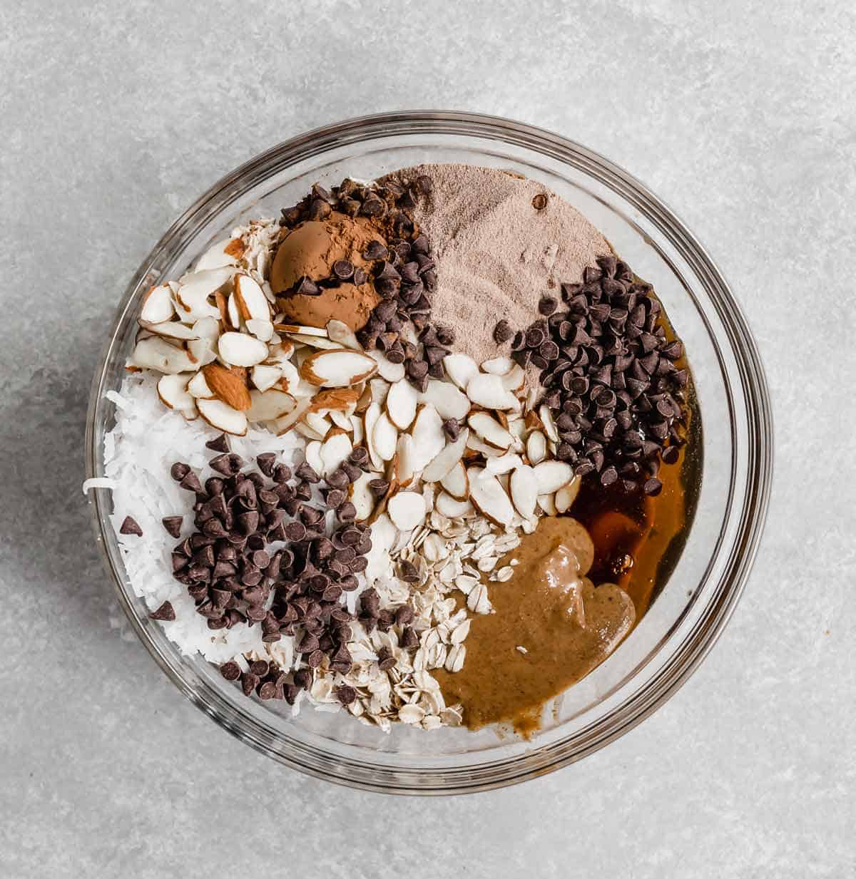 Almond Joy Protein Ball ingredients in a glass bowl on a light gray background.