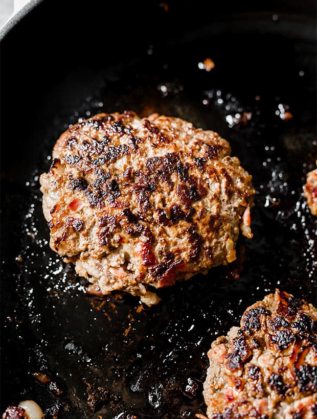 A skillet with beautifully browned bacon burgers.