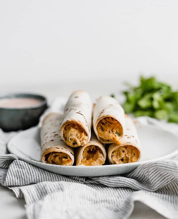 A plate with baked chicken taquitos on it.