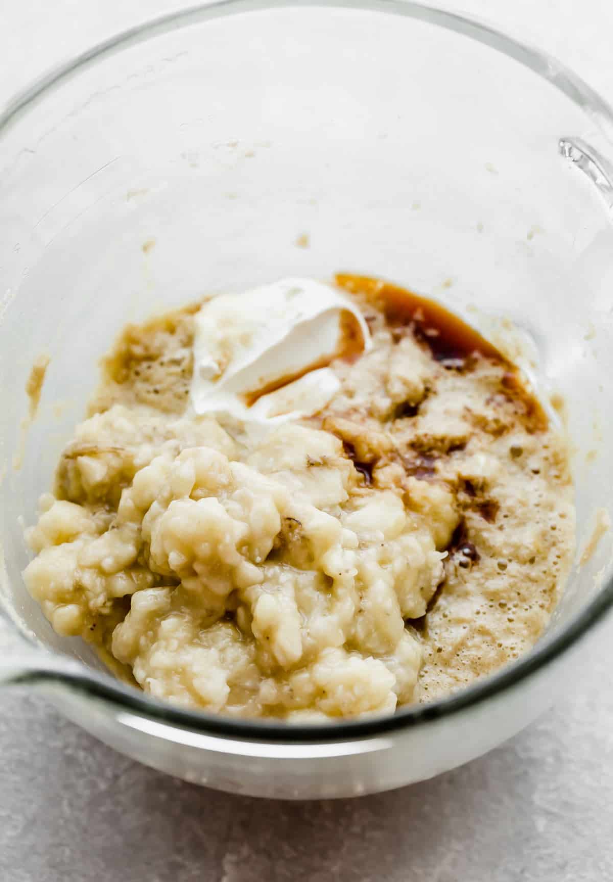 Mashed bananas, sour cream, and other Banana Bread Recipe ingredients in a glass mixing bowl.