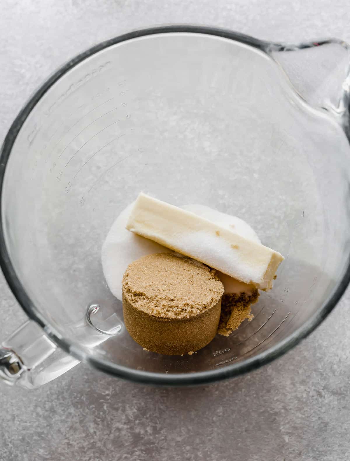 A glass bowl with a cube of butter, brown sugar, and sugar in it.