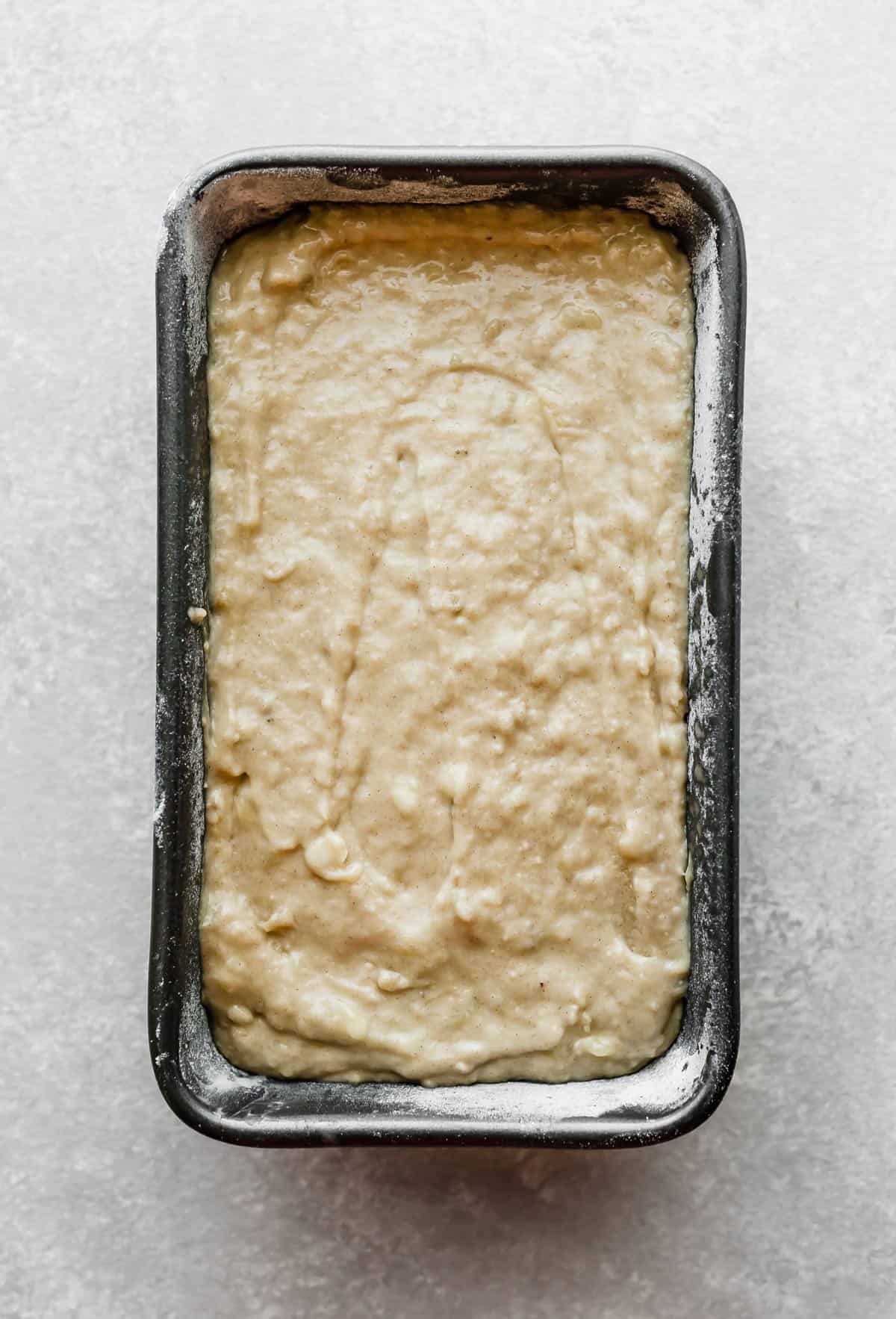 Banana bread batter in a grey bread pan on a light grey background.