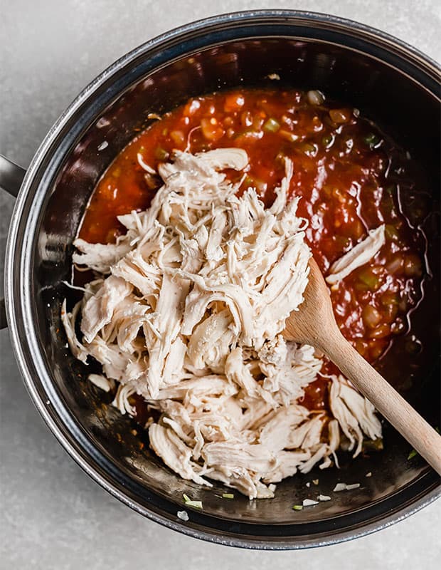 Shredded chicken in a large pot with BBQ chicken sandwich sauce.