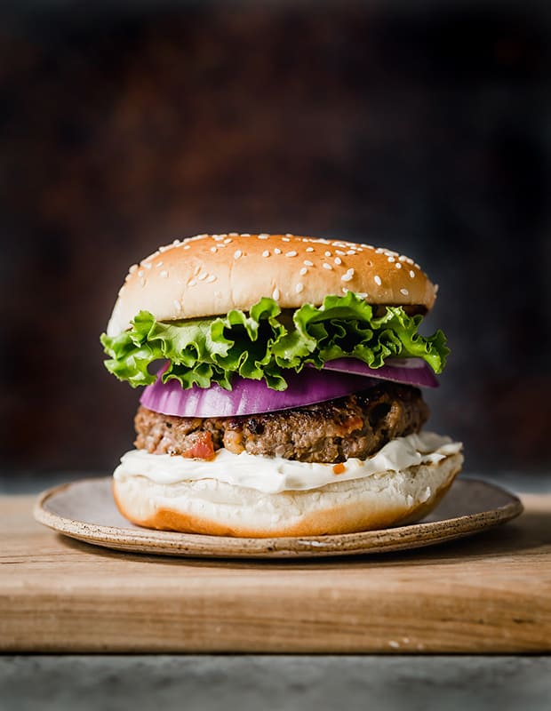 A bacon burger on a hamburger bun, with layers of lettuce and purple onion.