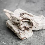 Three cookies and cream popsicles on top of each other, with a bite taken out of the top popsicle.