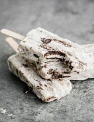 Three cookies and cream popsicles on top of each other, with a bite taken out of the top popsicle.