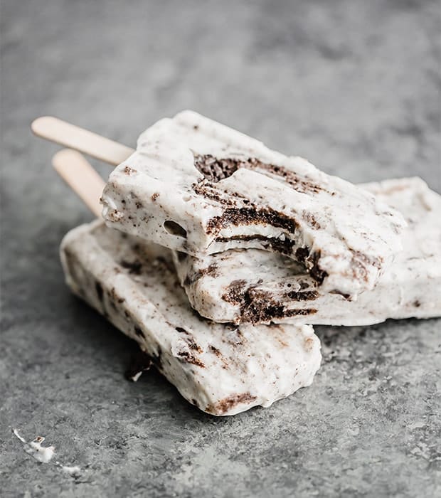 Three cookies and cream popsicles on top of each other, with a bite taken out of the top popsicle.