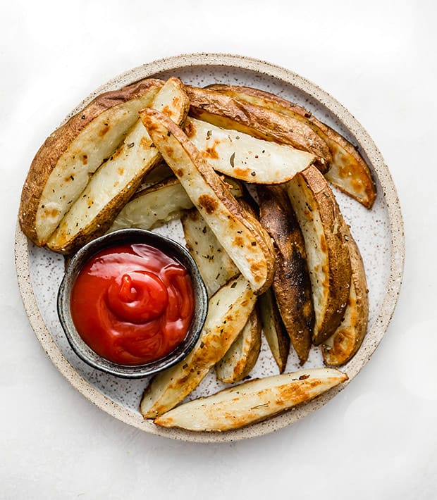 A plate of Crispy Baked Potato Wedges with a small bowl of ketchup.
